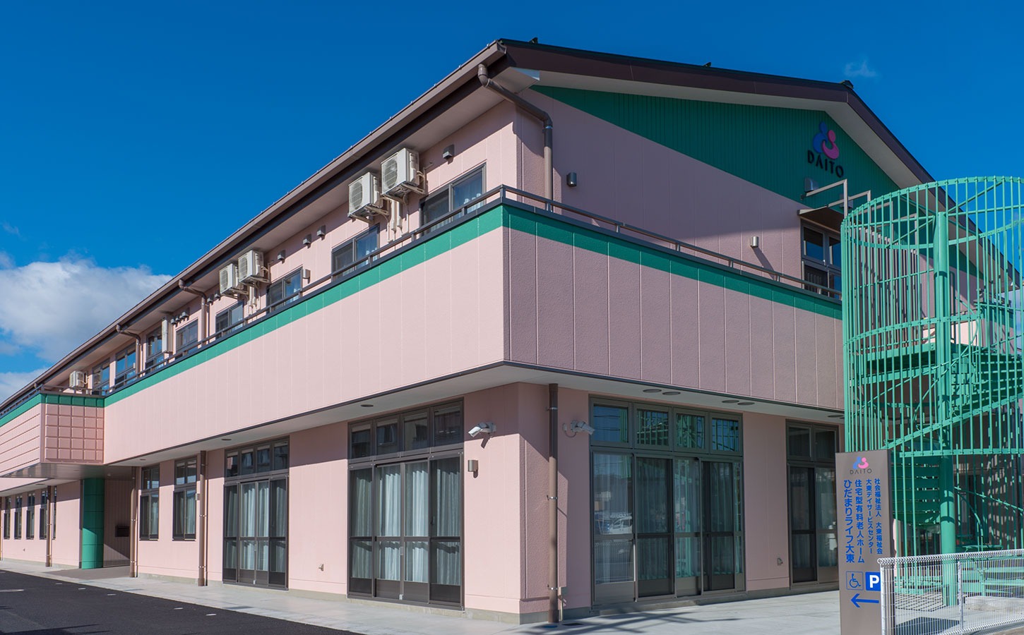 緑と白のツートンカラーの介護施設の建物外観。晴天下での全景撮影。